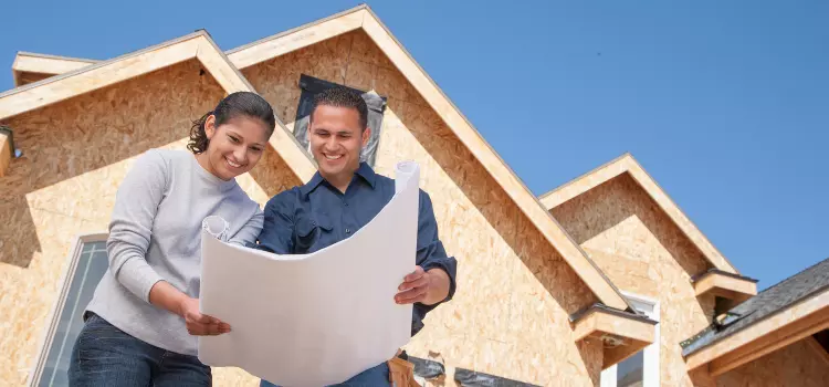Two people looking at house plans with a new house being built behind them.