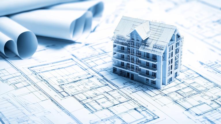 A 3D model of a housing building sits on top of building plans